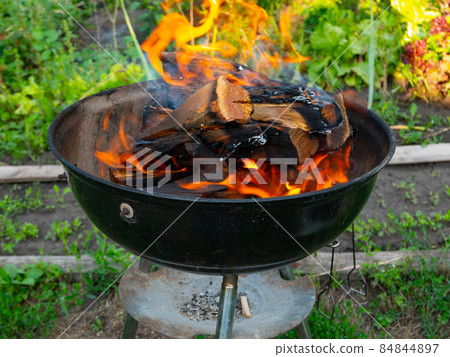 Freshly lit barbecue fire with logs of burning wood over small chips of kindling in a portable BBQ 84844897