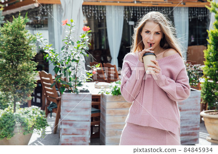 beautiful blonde woman with a hot drink with a straw on the street of the city 84845934