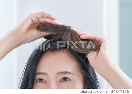 The head of a middle-aged woman trying to put a wig on her head in the mirror 84847536