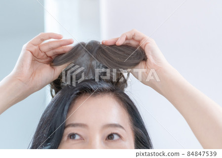 The head of a middle-aged woman trying to put a wig on her head in the mirror 84847539
