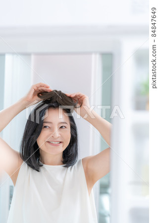 The head of a middle-aged woman trying to put a wig on her head in the mirror 84847649