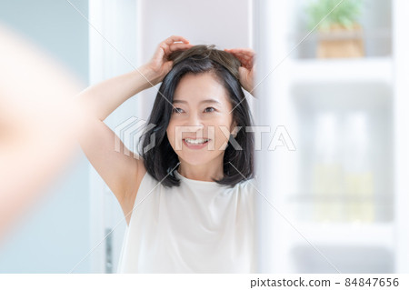 一個中年婦女的頭，試圖在鏡子裡給她的頭戴上假髮 84847656