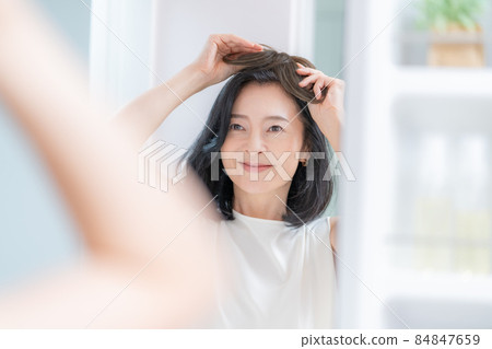 一個中年婦女的頭,試圖在鏡子裡給她的頭戴上假髮 一個中年婦女的頭,試圖在鏡子裡給她的頭戴上假髮 84847659