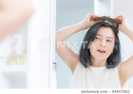 The head of a middle-aged woman trying to put a wig on her head in the mirror 84847662