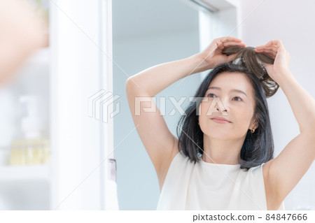 The head of a middle-aged woman trying to put a wig on her head in the mirror 84847666