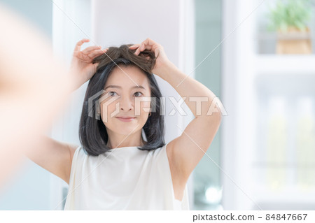 The head of a middle-aged woman trying to put a wig on her head in the mirror 84847667