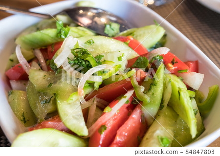 Tomato and cucumber salad with onion, pepper and parsly 84847803