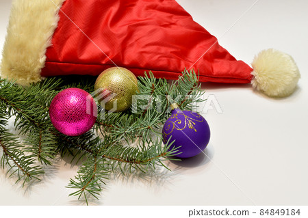 Three glass balls and a Santa Claus hat lie on a white table. Three glass balls and a Santa Claus hat lie on a white table. 84849184