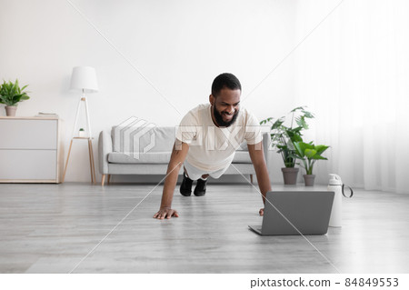 Cheerful millennial black bearded man does push-ups on mat on floor in room interior 84849553