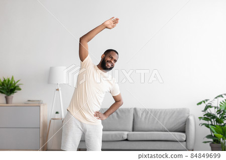 Happy young african american man with beard in white sportswear doing exercise and warm-up Happy young african american man with beard in white sportswear doing exercise and warm-up 84849699