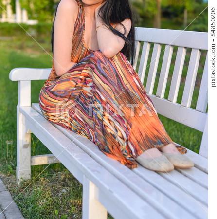 beautiful brunette model with long hair is having a photo shooting in the park. the woman is wearing an orange long summer dress beautiful brunette model with long hair is having a photo shooting in the park. the woman is wearing an orange long summer dress 84850206