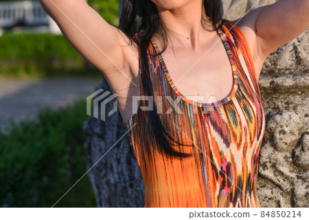 beautiful brunette model with long hair is having a photo shooting in the park. the woman is wearing an orange long summer dress 84850214