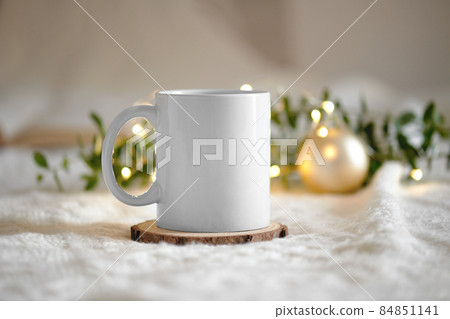 Mug mockup on a beige knited background with opened book and christmas garland lights, cozy winter day at hugge home 84851141