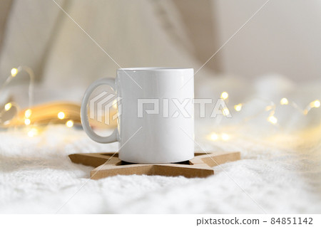 Mug mockup on a beige knited background with opened book and christmas garland lights, cozy winter day at hugge home 84851142