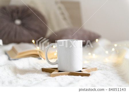 Mug mockup on a beige knited background with opened book and christmas garland lights, cozy winter day at hugge home Mug mockup on a beige knited background with opened book and christmas garland lights, cozy winter day at hugge home 84851143