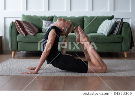 Woman working out at home, arching her back and reaching her toes for her head. Woman working out at home, arching her back and reaching her toes for her head. 84853369