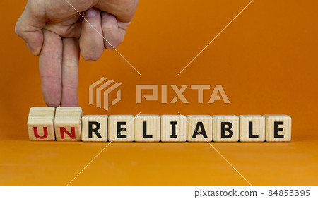 Unreliable or reliable symbol. Businessman turns wooden cubes and changes the word unreliable to reliable. Beautiful orange background, copy space. Business and unreliable or reliable concept. 84853395