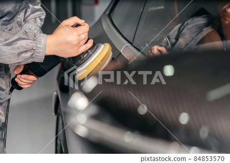 Worker polishing car with special grinder and wax from scratches at the car service station. Professional car detailing and maintenance concept Worker polishing car with special grinder and wax from scratches at the car service station. Professional car detailing and maintenance concept 84853570