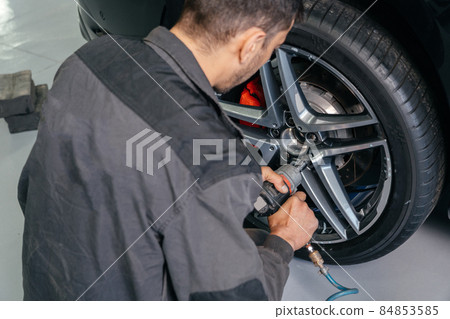 Mechanic changing car wheel in auto repair shop using an electric drill to loosen the bolts .concept of service or replacement. 84853585