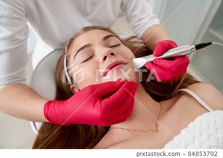 Cosmetologist making hardware cleaning of the face of beautiful young patient. Concept skin cleansing and restoration of elasticity 84853702
