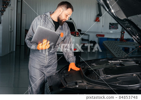 Car mechanic working with a laptop in Auto Repair Service checking car engine Car mechanic working with a laptop in Auto Repair Service checking car engine 84853748
