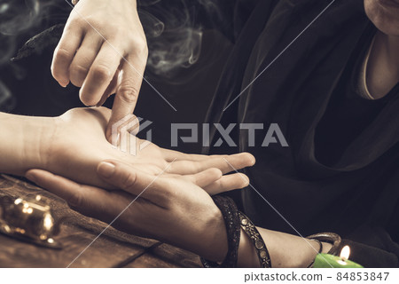 The witch is a fortune teller reading a good luck close-up. The fortune teller draws lines on the client's hand 84853847