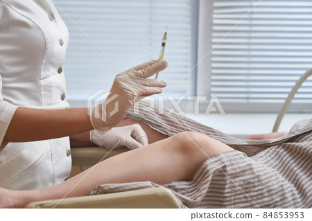 Gynecologist with syringe makes an injection to patient in gynecology chair Gynecologist with syringe makes an injection to patient in gynecology chair 84853953