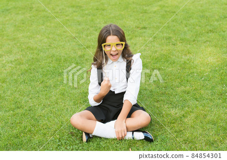Small schoolgirl sit on green grass. Fashion accessory. Small schoolgirl sit on green grass. Fashion accessory. 84854301