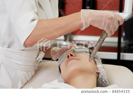Young woman receiving laser treatment in cosmetology clinic Young woman receiving laser treatment in cosmetology clinic 84854335
