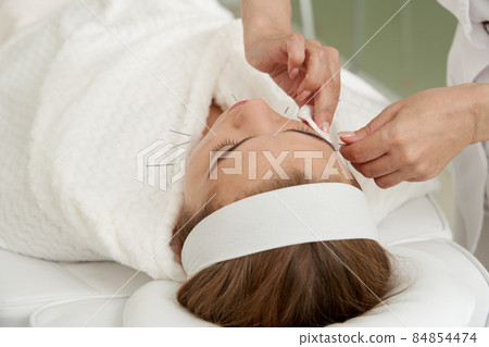 Doctor puts needles into female face on the acupuncture treatment therapy in spa salon. Alternative Medicine concept Doctor puts needles into female face on the acupuncture treatment therapy in spa salon. Alternative Medicine concept 84854474