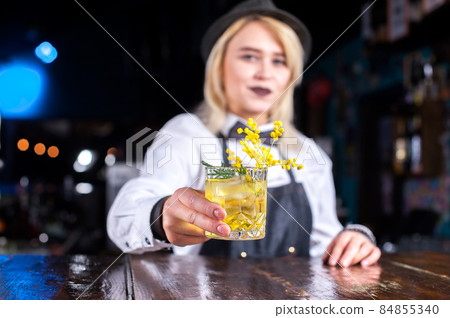 Charming girl mixologist decorates colorful concoction behind bar Charming girl mixologist decorates colorful concoction behind bar 84855340