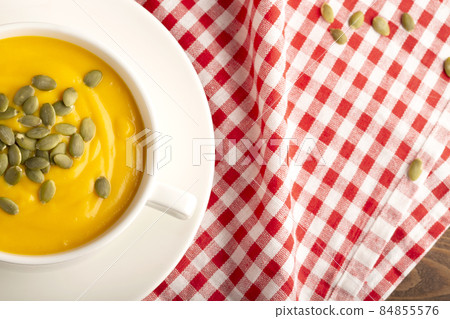 Pumpkin soup with cream and pumpkin seeds. background with red fabric. Free space, closeup. Flat lay. Pumpkin soup with cream and pumpkin seeds. background with red fabric. Free space, closeup. Flat lay. 84855576