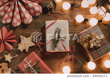 Sustainable gift wrapping flat lay, gift boxes packed and decorated with kraft paper, string and dried flowers surrounded by LED bulb lights on wooden table Sustainable gift wrapping flat lay, gift boxes packed and decorated with kraft paper, string and dried flowers surrounded by LED bulb lights on wooden table 84856271