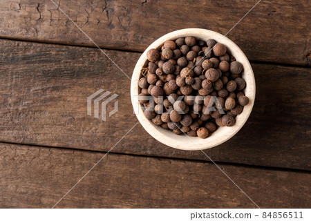 Dried allspice in bowl on wooden table. Close up. Top view 84856511