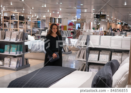 Female customer in casual clothes inspecting bed with bedclothes while shopping in spacious contemporary mall Female customer in casual clothes inspecting bed with bedclothes while shopping in spacious contemporary mall 84856855