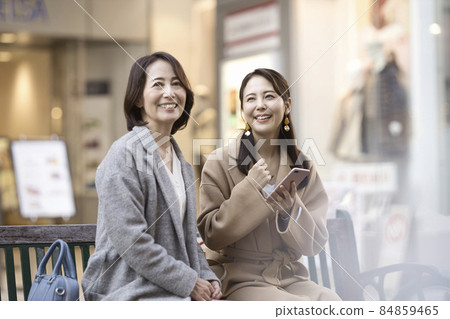 Two women wearing coats and looking at smartphones 84859465