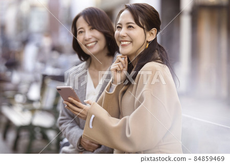 Two women wearing coats and looking at smartphones 84859469