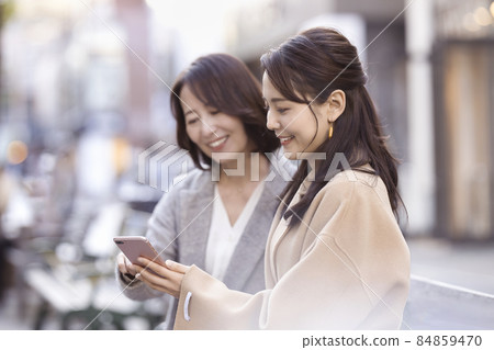 Two women wearing coats and looking at smartphones 84859470