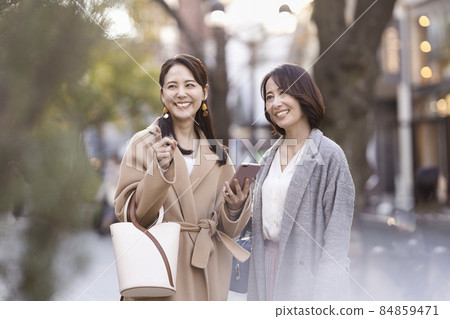 兩個女人穿著外套,看著智能手機 兩個女人穿著外套,看著智能手機 84859471