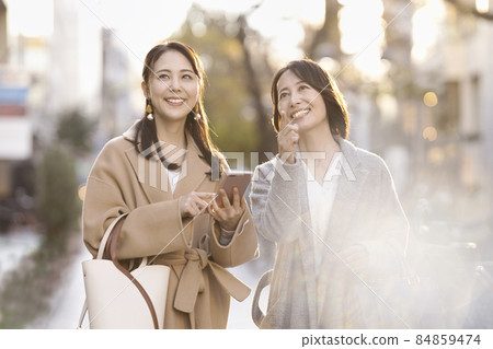 兩個女人穿著外套，看著智能手機 84859474