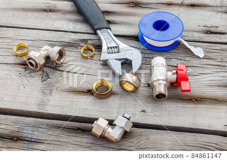Various plumbing spare parts, sealing tape and adjustable wrench on rustic wooden background 84861147