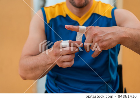 a person with a disability puts on a corset and bandages on his arms and fingers in preparation for a game in the arena a person with a disability puts on a corset and bandages on his arms and fingers in preparation for a game in the arena 84861416