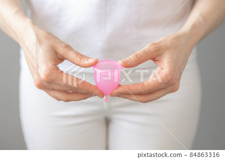 a European woman holds a pink menstrual cup made of silicone in her hands 84863316