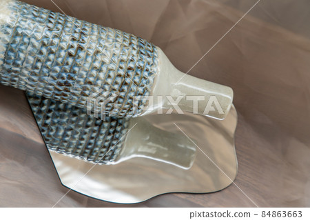 Handmade ceramic vase bottle shape on mirror on fabric textured table cloth. Handmade ceramic vase bottle shape on mirror on fabric textured table cloth. 84863663