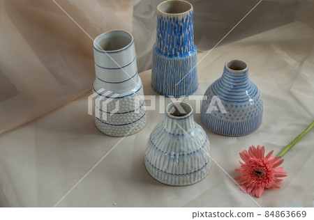 Four Blue and White handmade ceramic vase with Pink flower on Blush textured table cloth. Four Blue and White handmade ceramic vase with Pink flower on Blush textured table cloth. 84863669