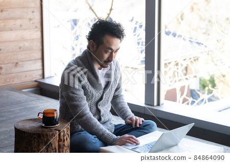 Japanese man working while doing remote work on a wooden deck in the countryside Japanese man working while doing remote work on a wooden deck in the countryside 84864090