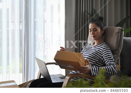 Young asian woman sitting in living room and opening parcel boxes. 84865593