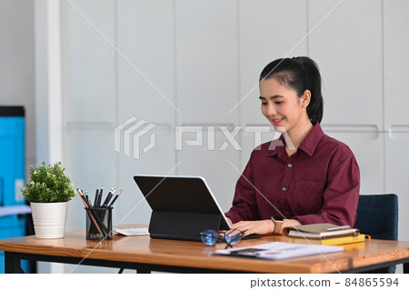 Charming businesswoman sitting in office and searching information on computer tablet. 84865594
