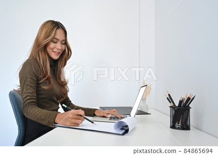 Attractive businesswoman checking information on paperwork and working with laptop computer. 84865694