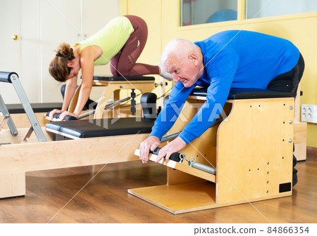 Elderly man doing remedial gymnastics on pilates combo chair 84866354